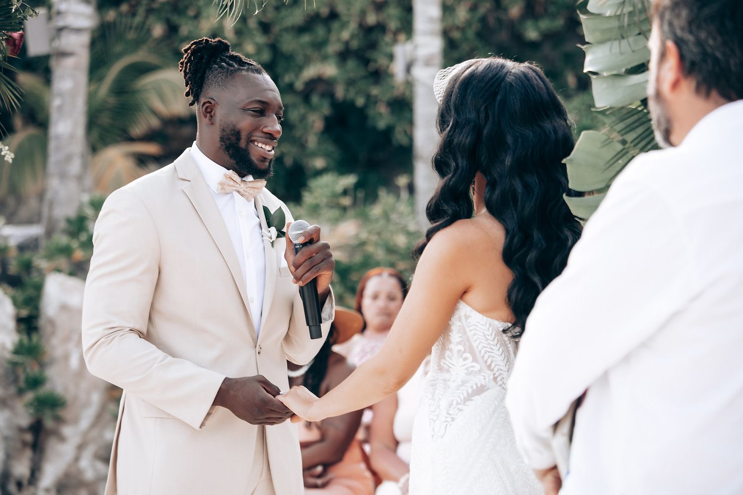 Wedding ceremony in progress with guests seated outdoors under tropical foliage.