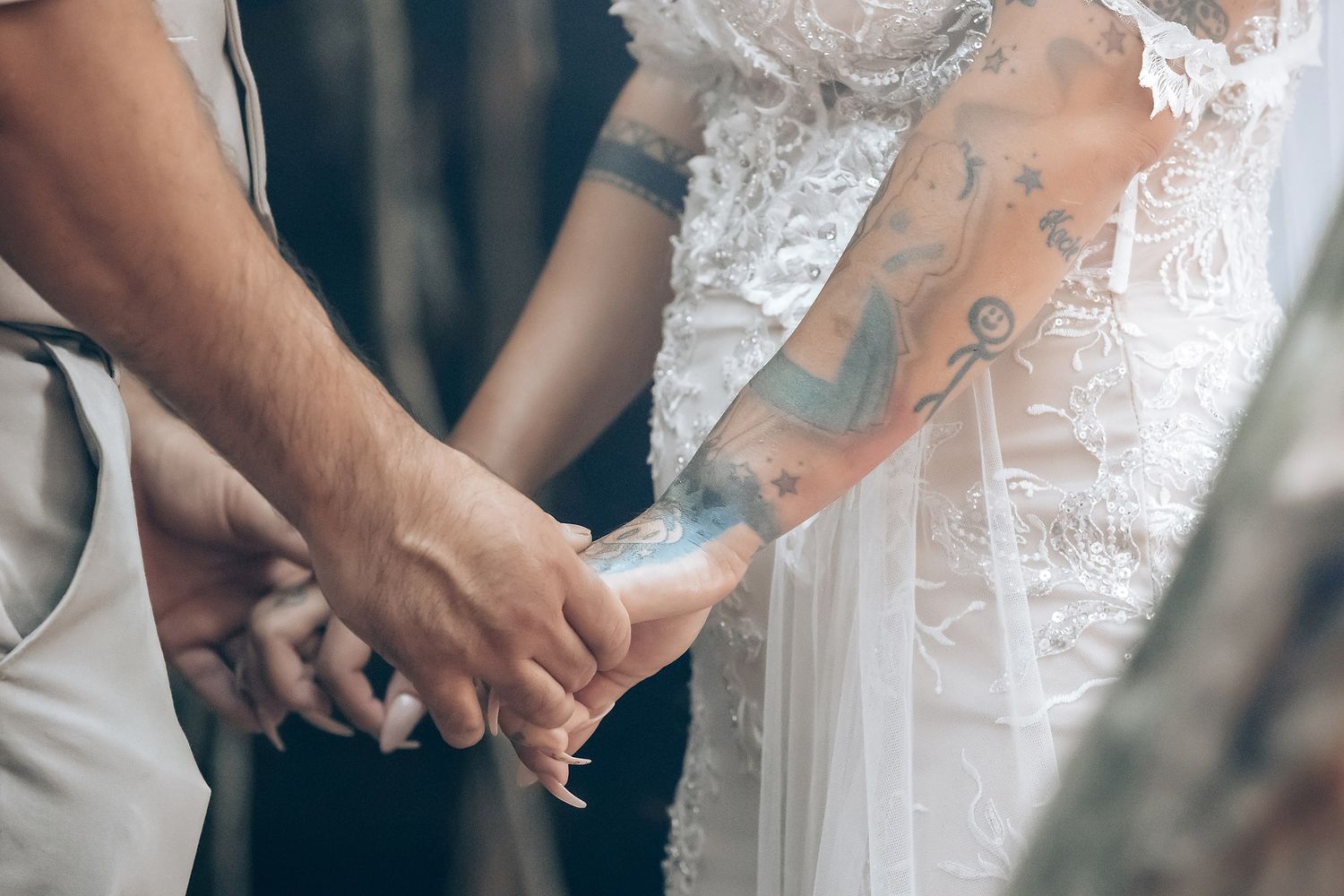 Close-up of couple holding hands with delicate lace wedding dress details visible.