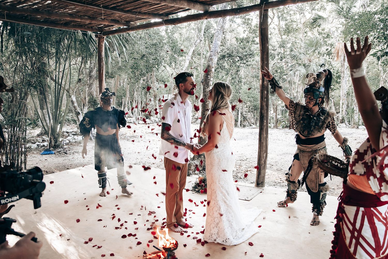 Wedding celebration with traditional Mayan dancers throwing rose petals under jungle canopy.