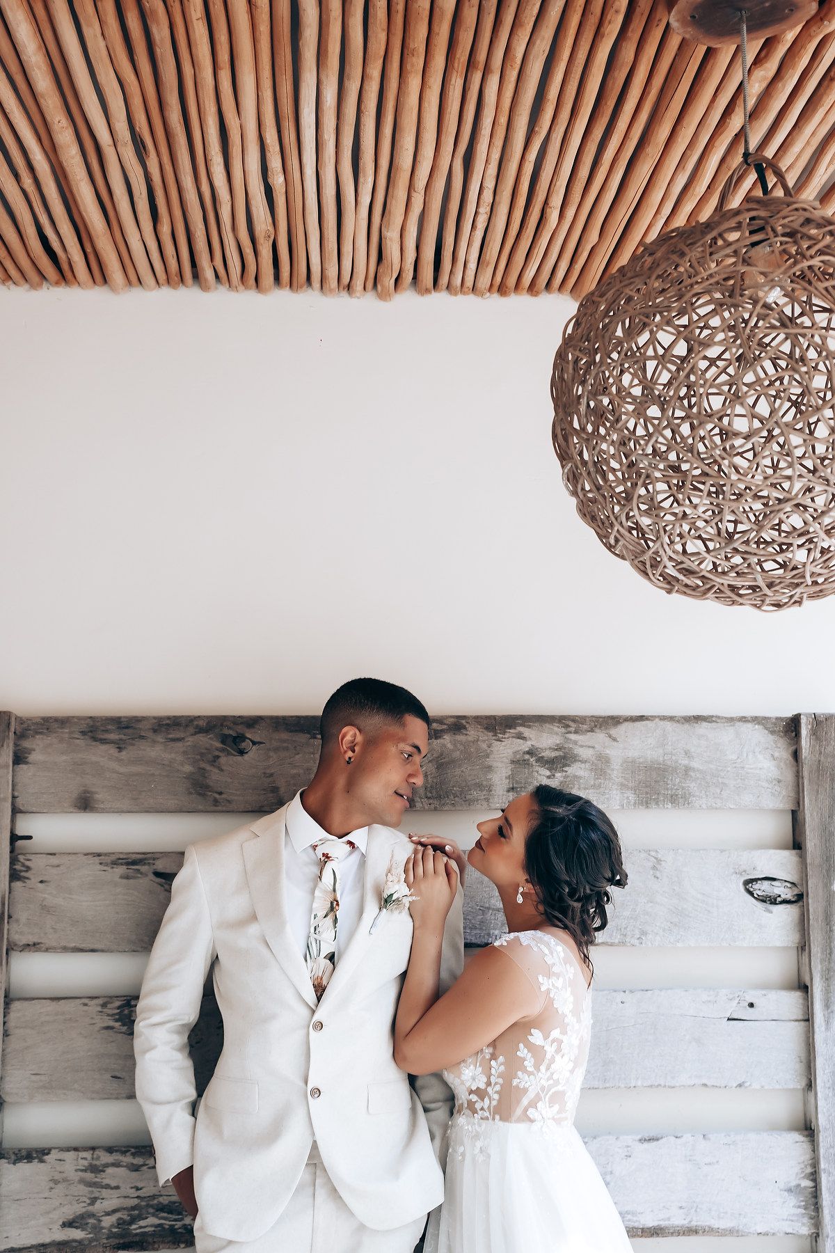 A romantic couple embraces under rustic wooden beams and woven pendant lights in an intimate wedding moment.
