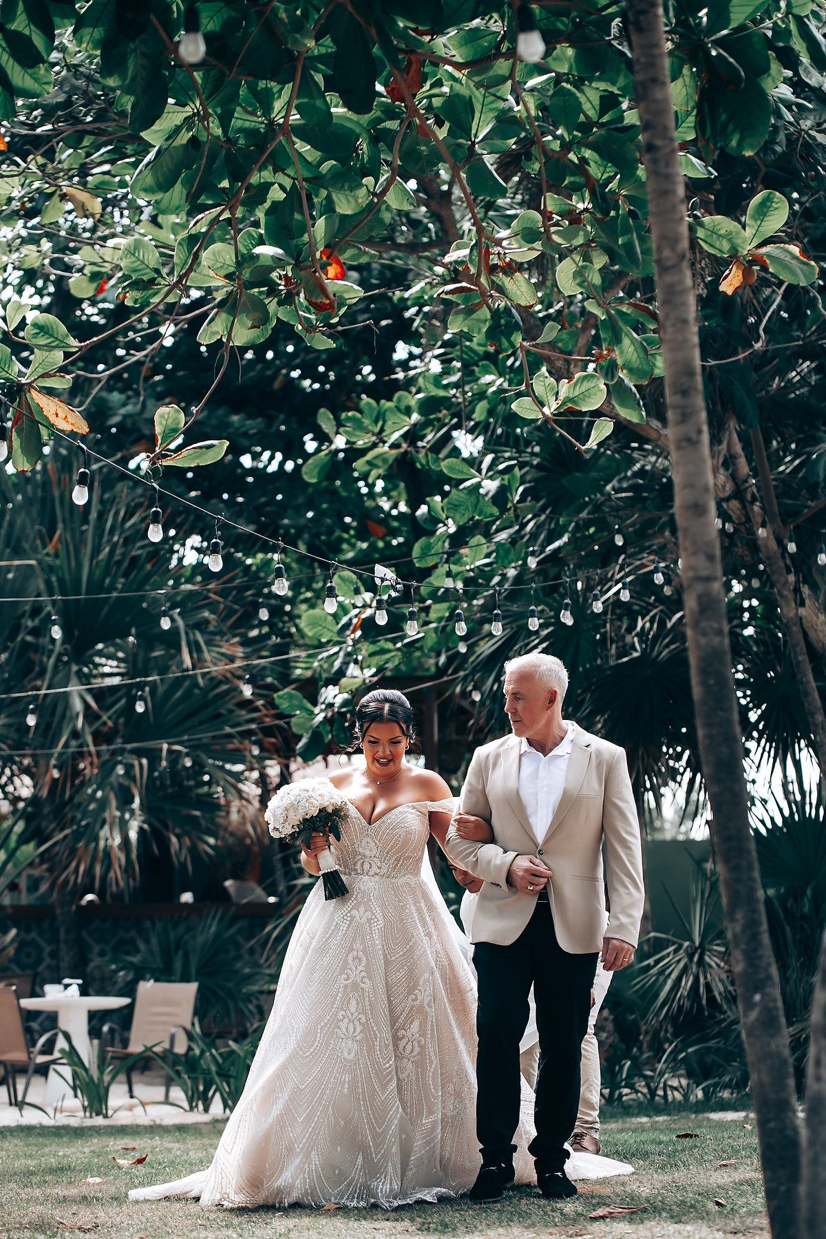 A romantic wedding photoshoot in a lush garden setting with palm trees and greenery.