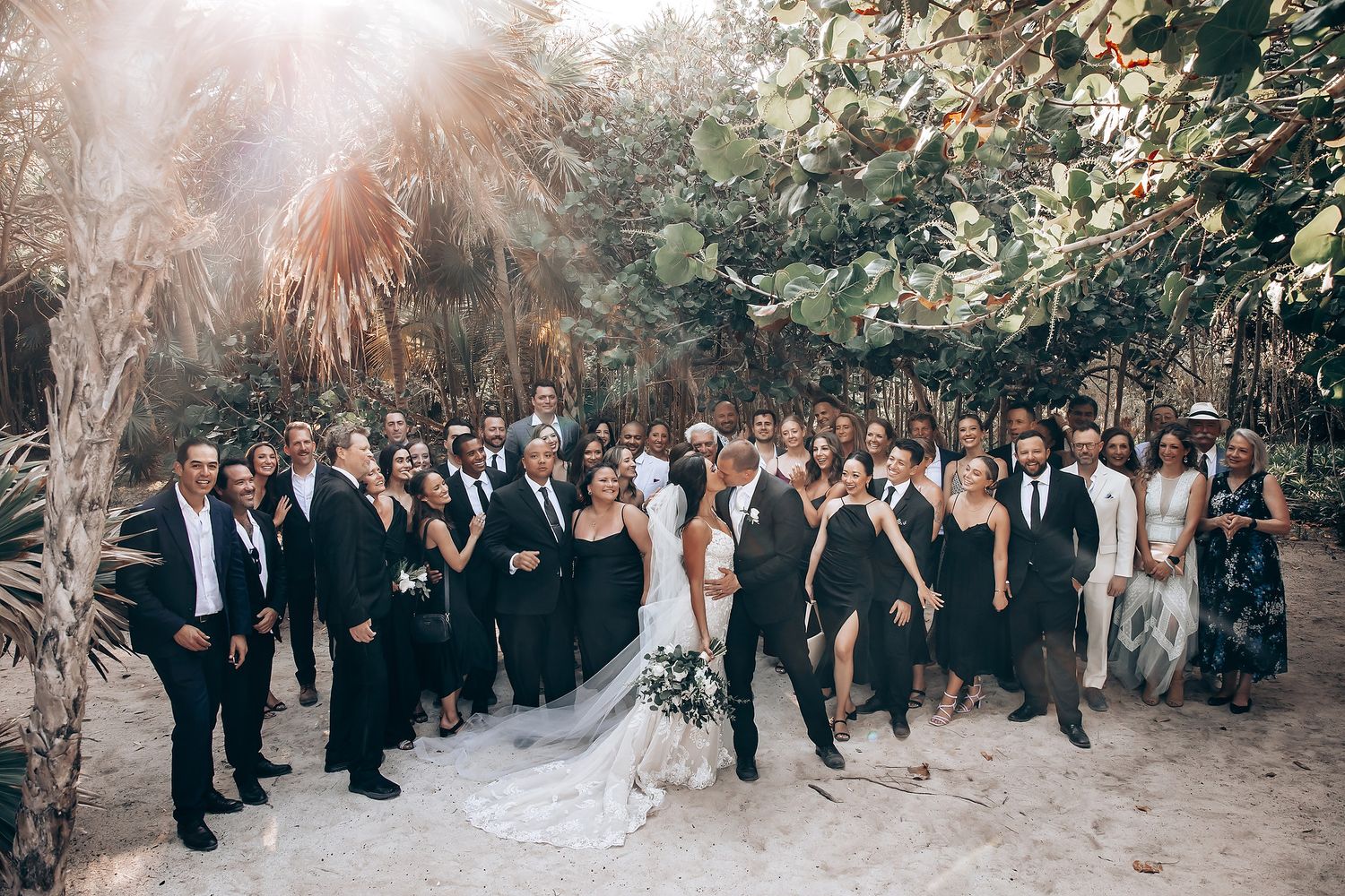 Wedding ceremony gathering in a sunlit outdoor garden setting with guests watching.