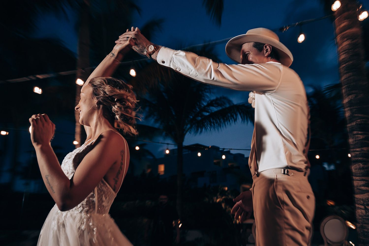 Dancing couple celebrates at their evening wedding reception under string lights.
