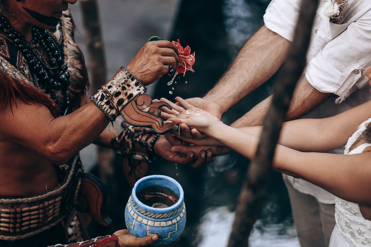 Hands participate in a traditional Mayan ceremony with a blue ceramic bowl and ritual objects.