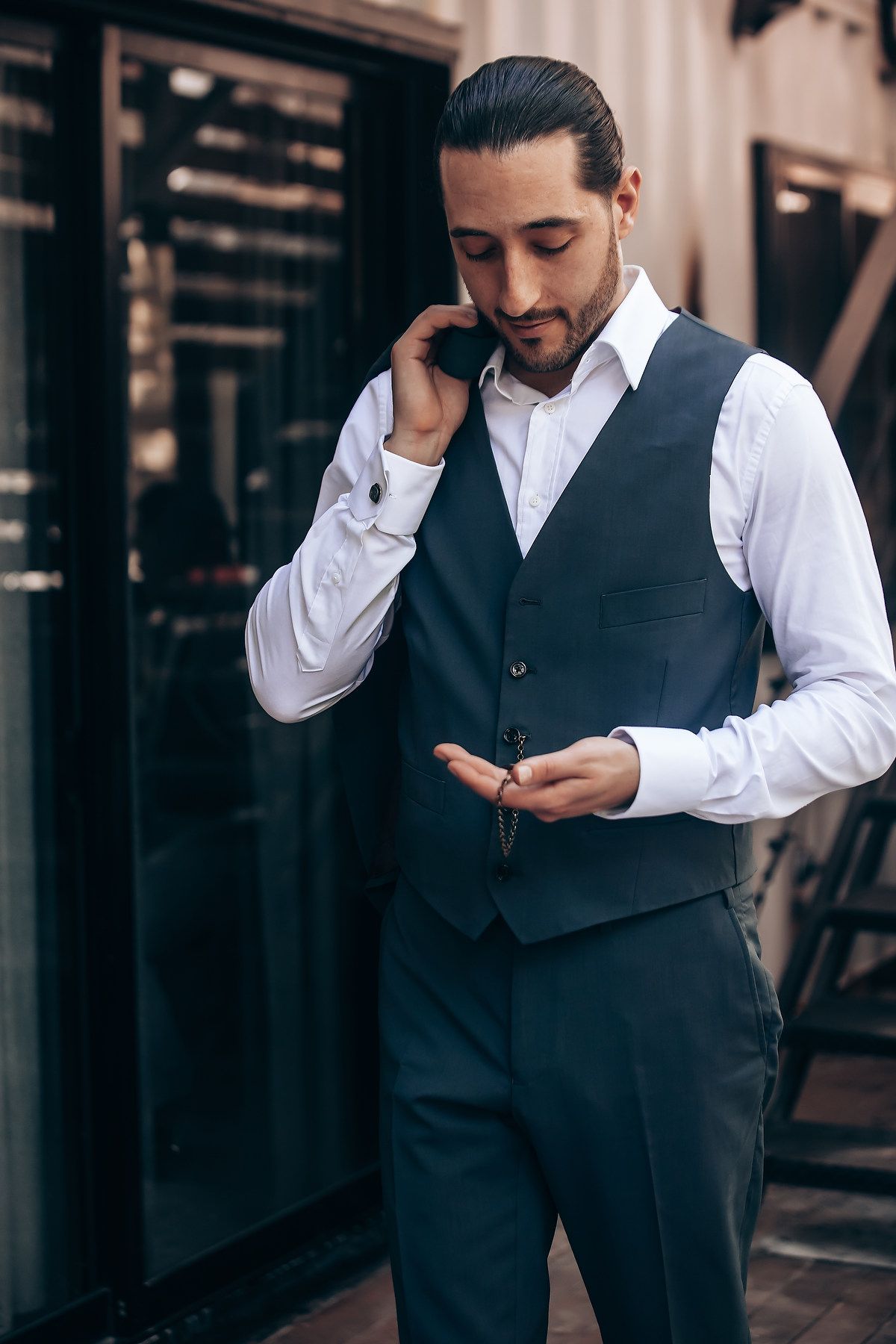 Groom in formal attire checks his phone while standing in an elegant setting.