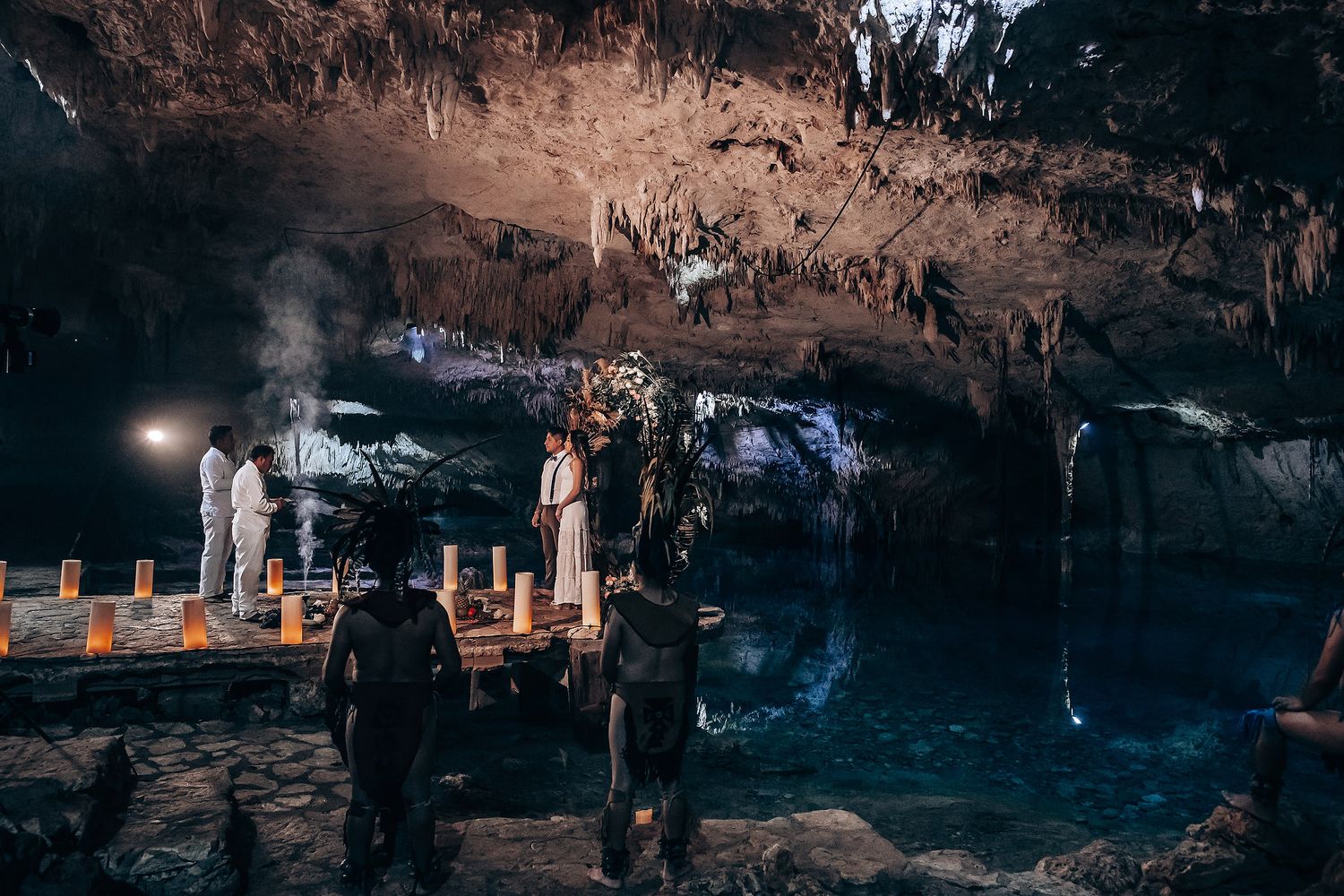 Visitors explore a dimly lit cave with illuminated rock formations and blue lighting creating an atmospheric underground scene.