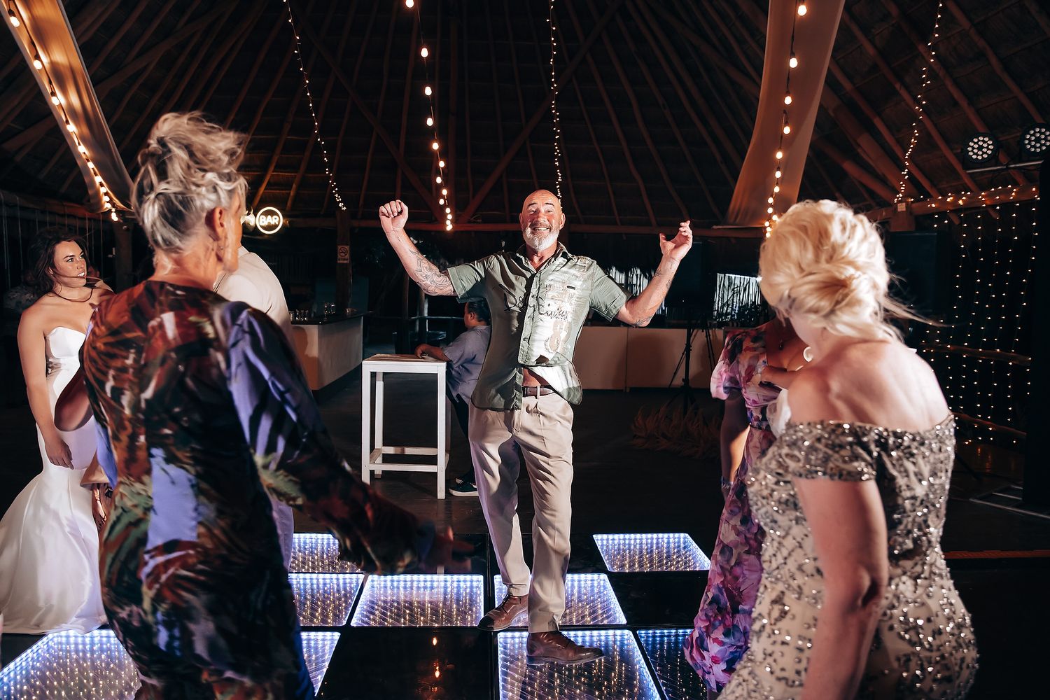 Wedding reception guests dancing and celebrating on a dance floor under string lights.