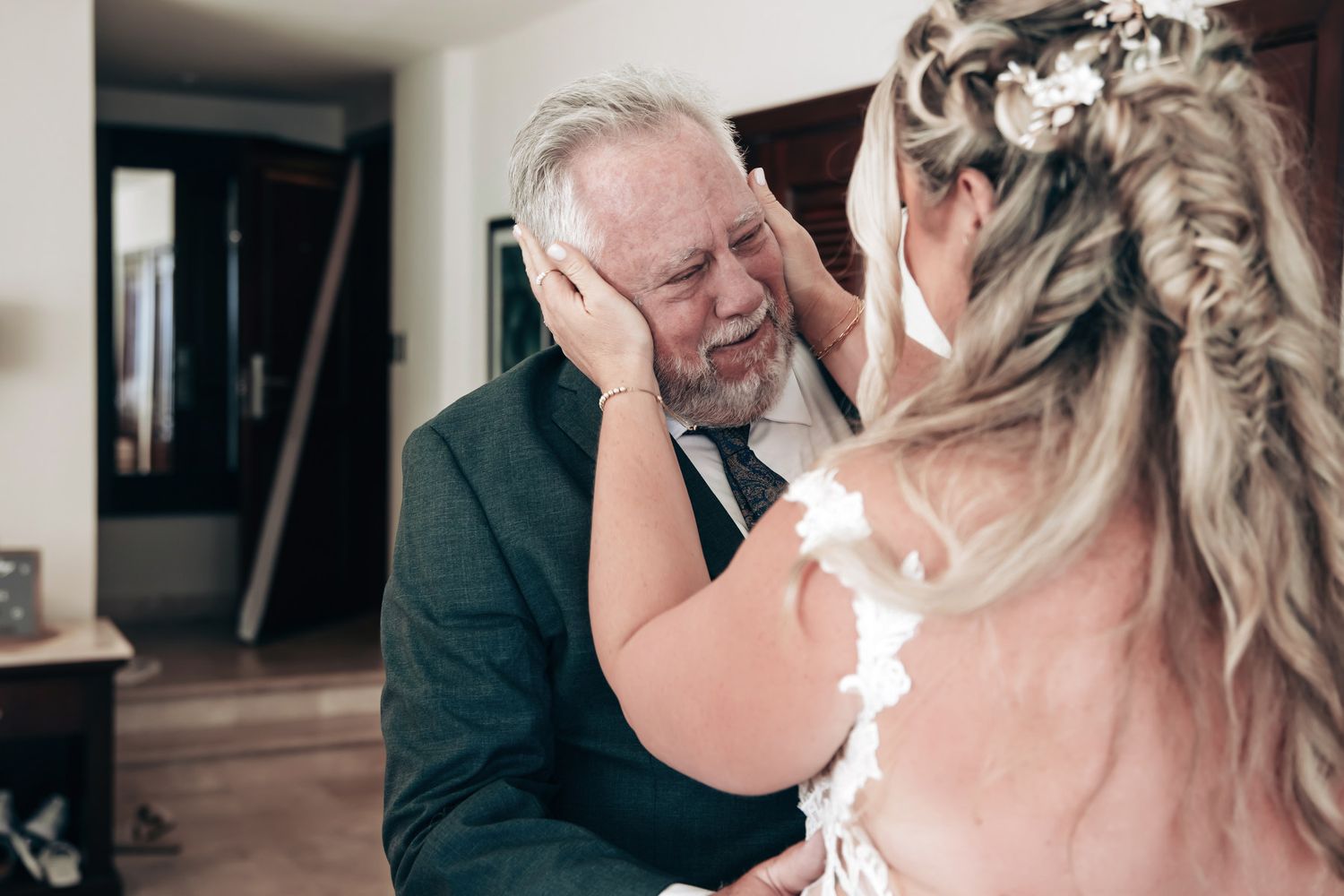 Emotional father-daughter first look moment with bride in white gown and floral hair accessory.