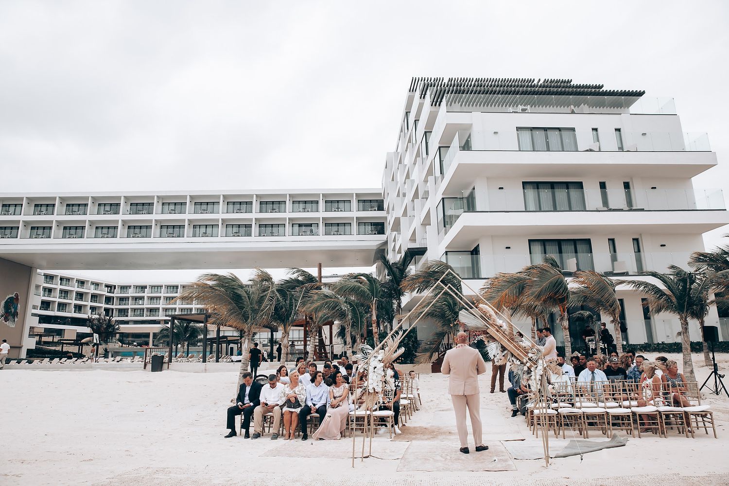 Modern beachfront resort venue with palm trees and wedding ceremony setup.