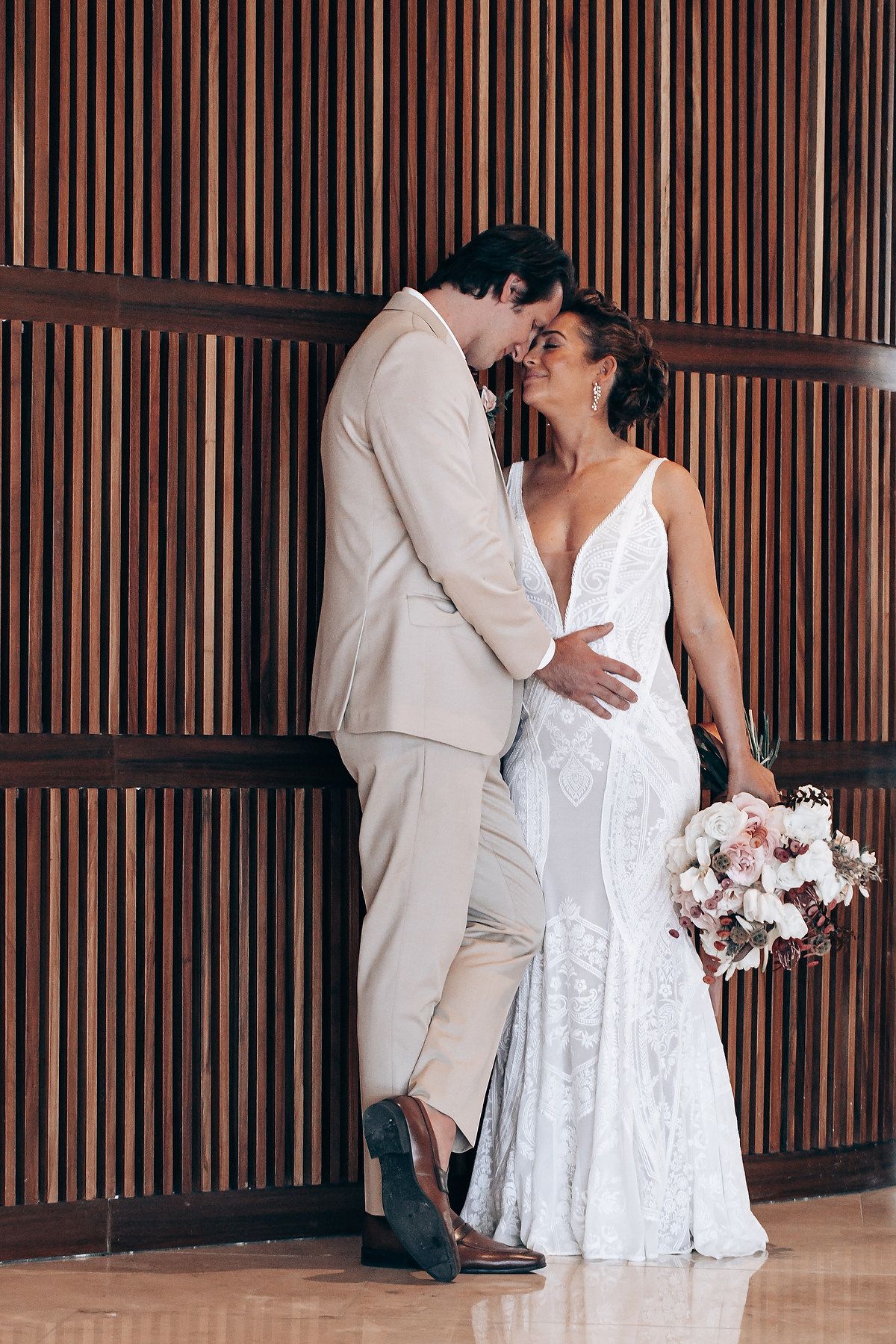 Couple in white attire sharing a romantic moment against a wooden slatted wall.
