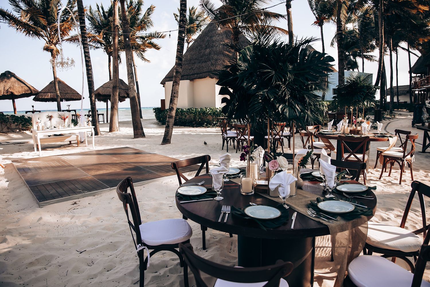 Beachfront wedding reception setup with palm trees and white decor against ocean backdrop.
