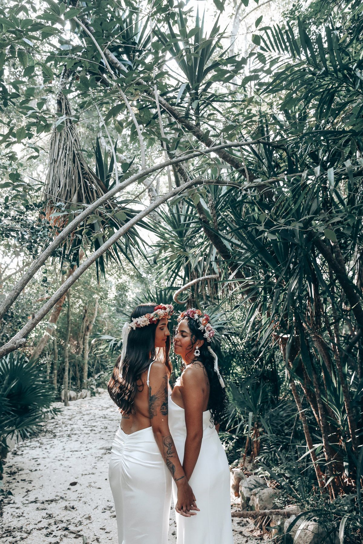 Two people in white dresses walk together through a palm-lined tropical path.