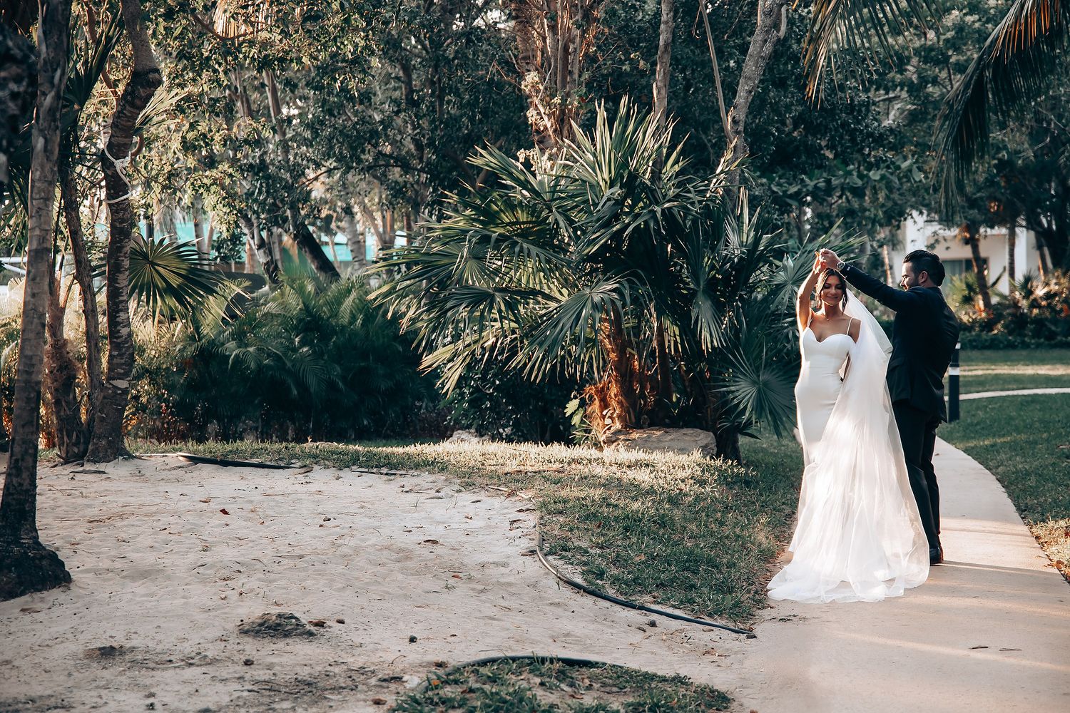 A couple shares a romantic moment on a palm tree-lined path during their wedding day.