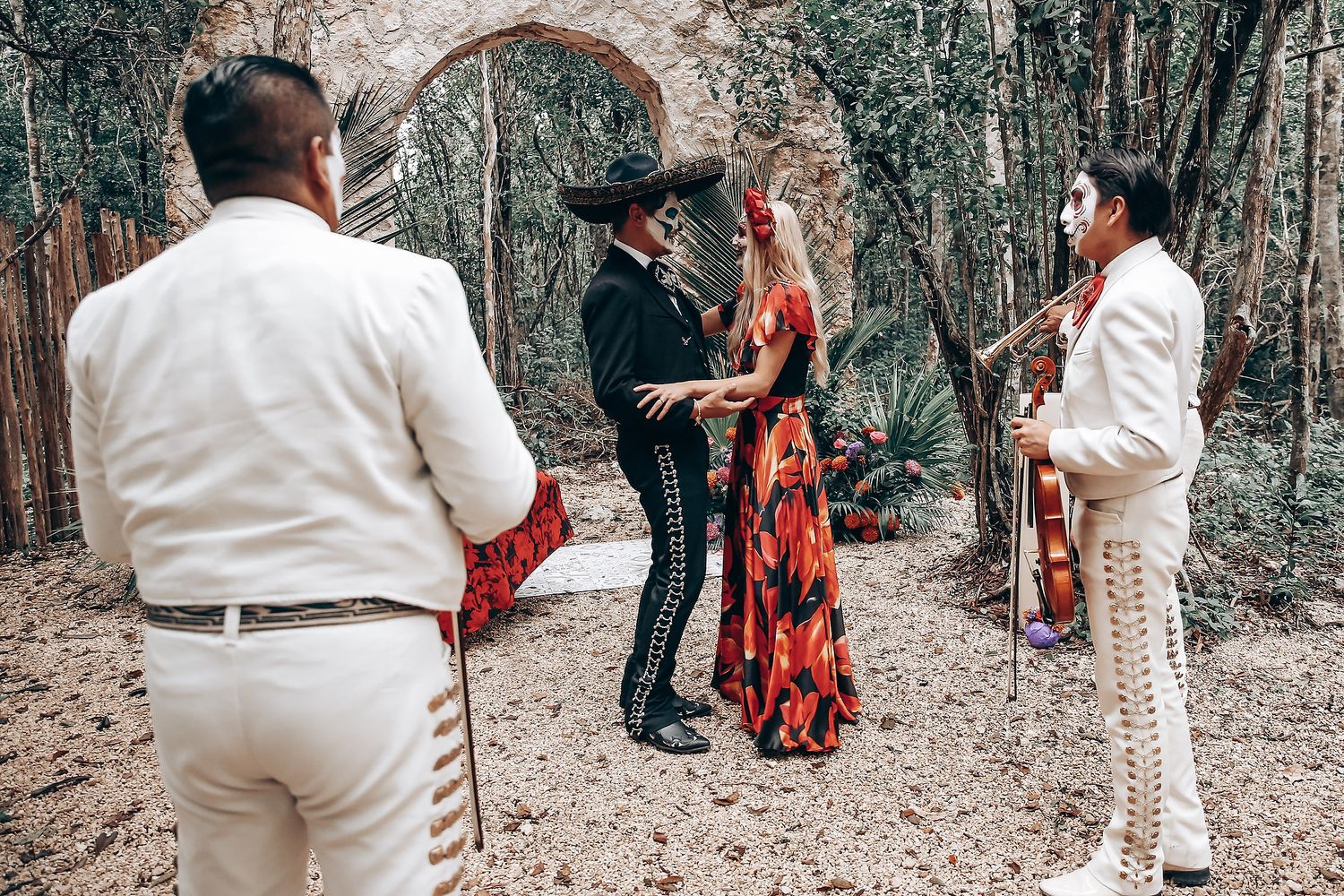 A couple in contrasting black and white outfits dance together in a wooded setting with dramatic lighting.