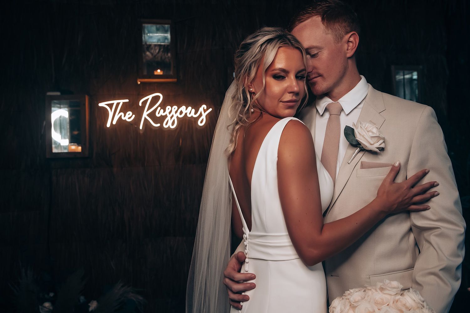 A couple shares a romantic dance moment at their wedding reception with a neon sign glowing in the background.