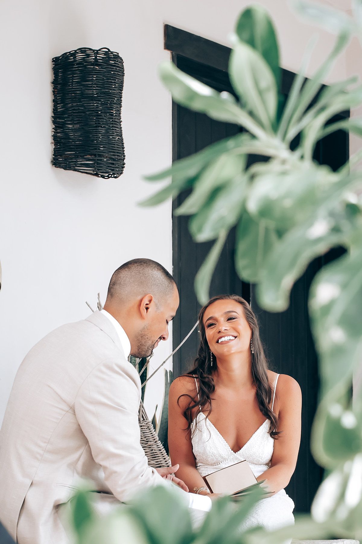 A romantic couple shares intimate moments in a tropical setting with lush green plants in the background.