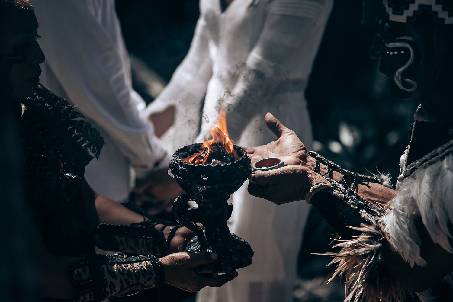 Hands holding a burning ceremonial flame in a dark moody setting during a ritual gathering.