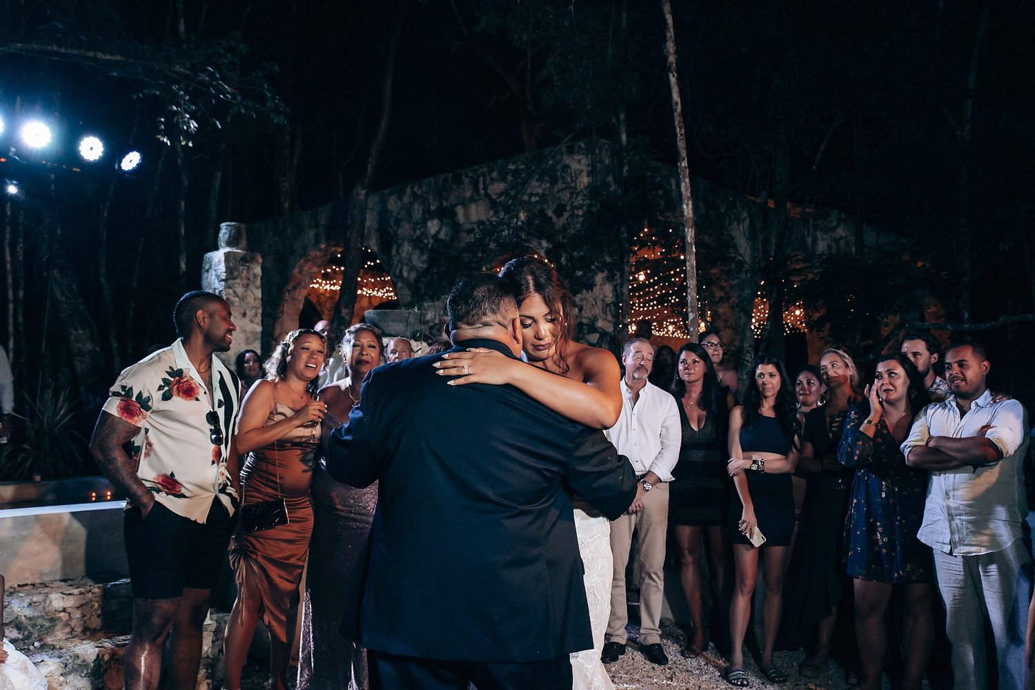 Evening wedding reception under trees with ambient lighting and dancing guests.