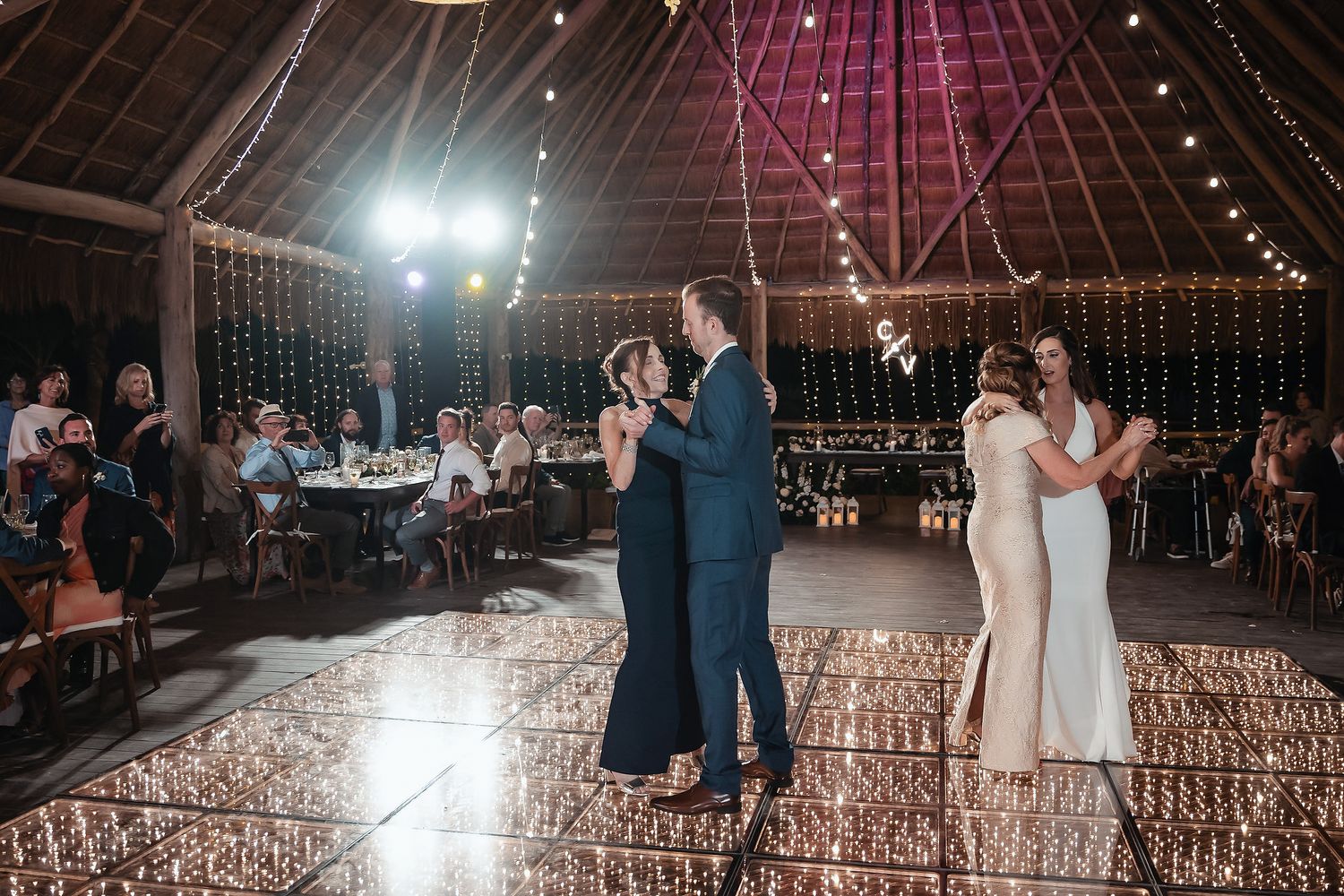 Couples share first dance on glowing dance floor in rustic barn wedding venue with string lights.