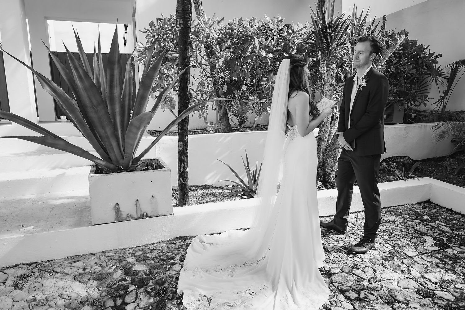 Black and white photo of a bride and groom sharing a first look moment in a lush garden courtyard.