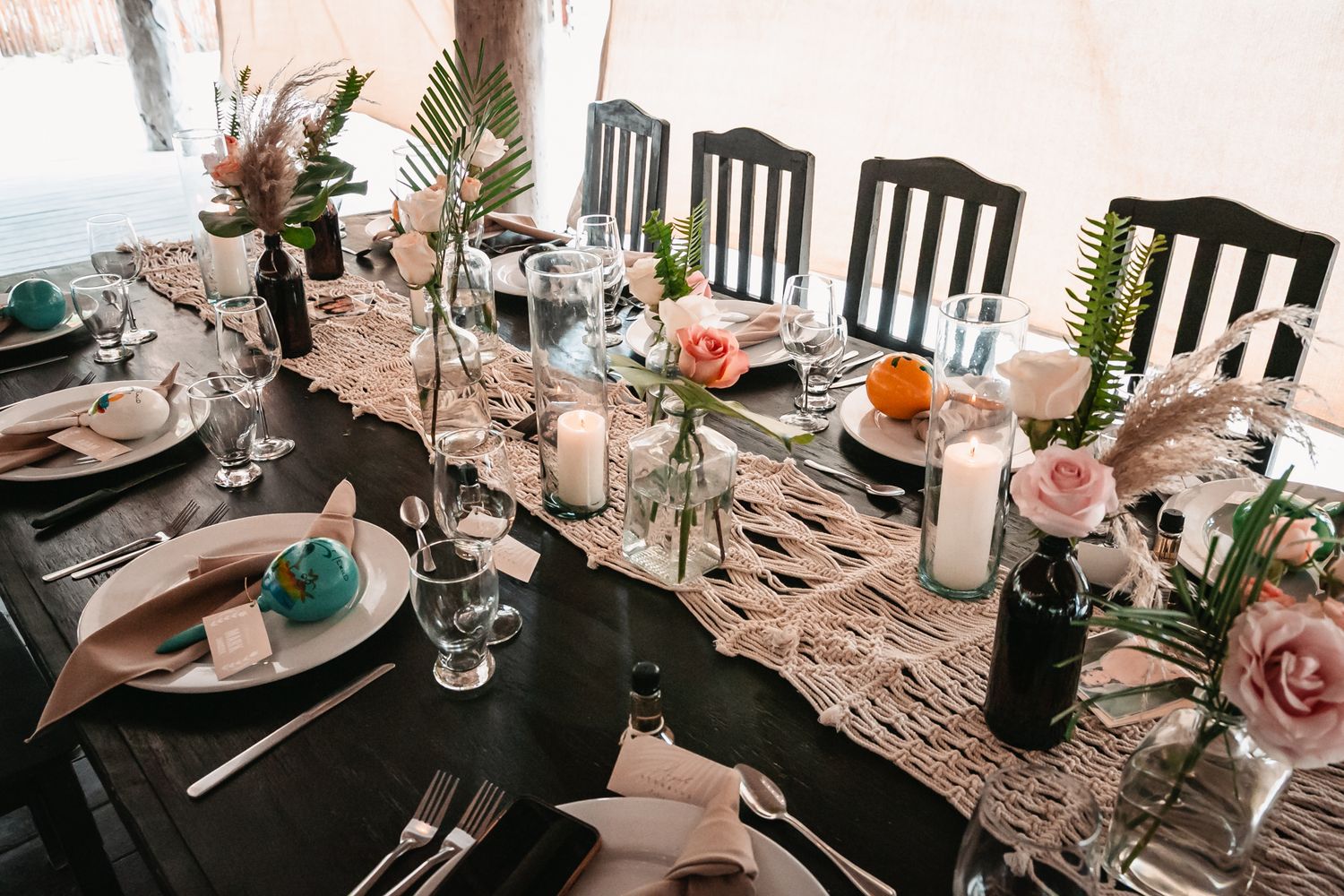 Boho wedding reception table with macrame runner, colorful flowers, and candles overhead.