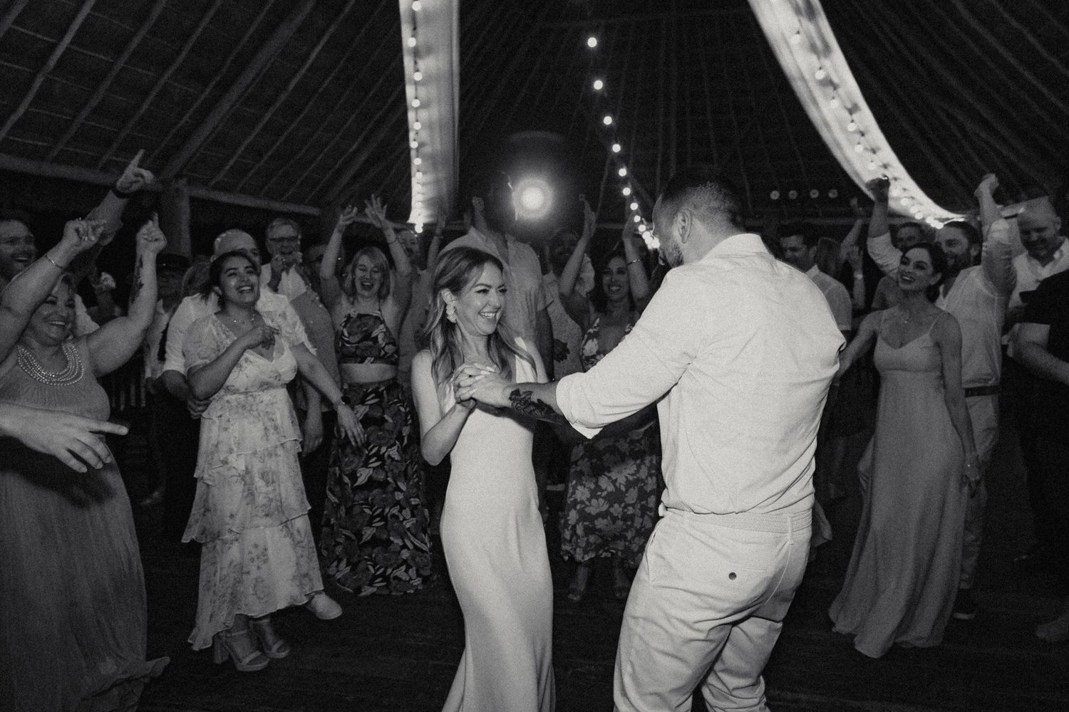 Bride and groom share a first dance surrounded by celebrating guests at reception.