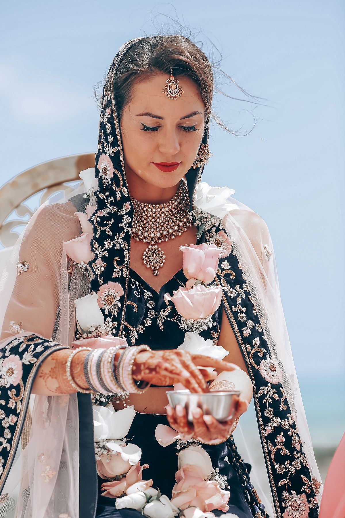 A person in traditional attire with intricate jewelry participates in a wedding ceremony ritual.