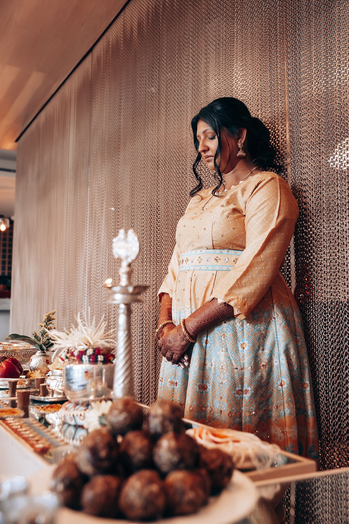 A person in traditional dress stands beside an elegant buffet table with decorative food displays.