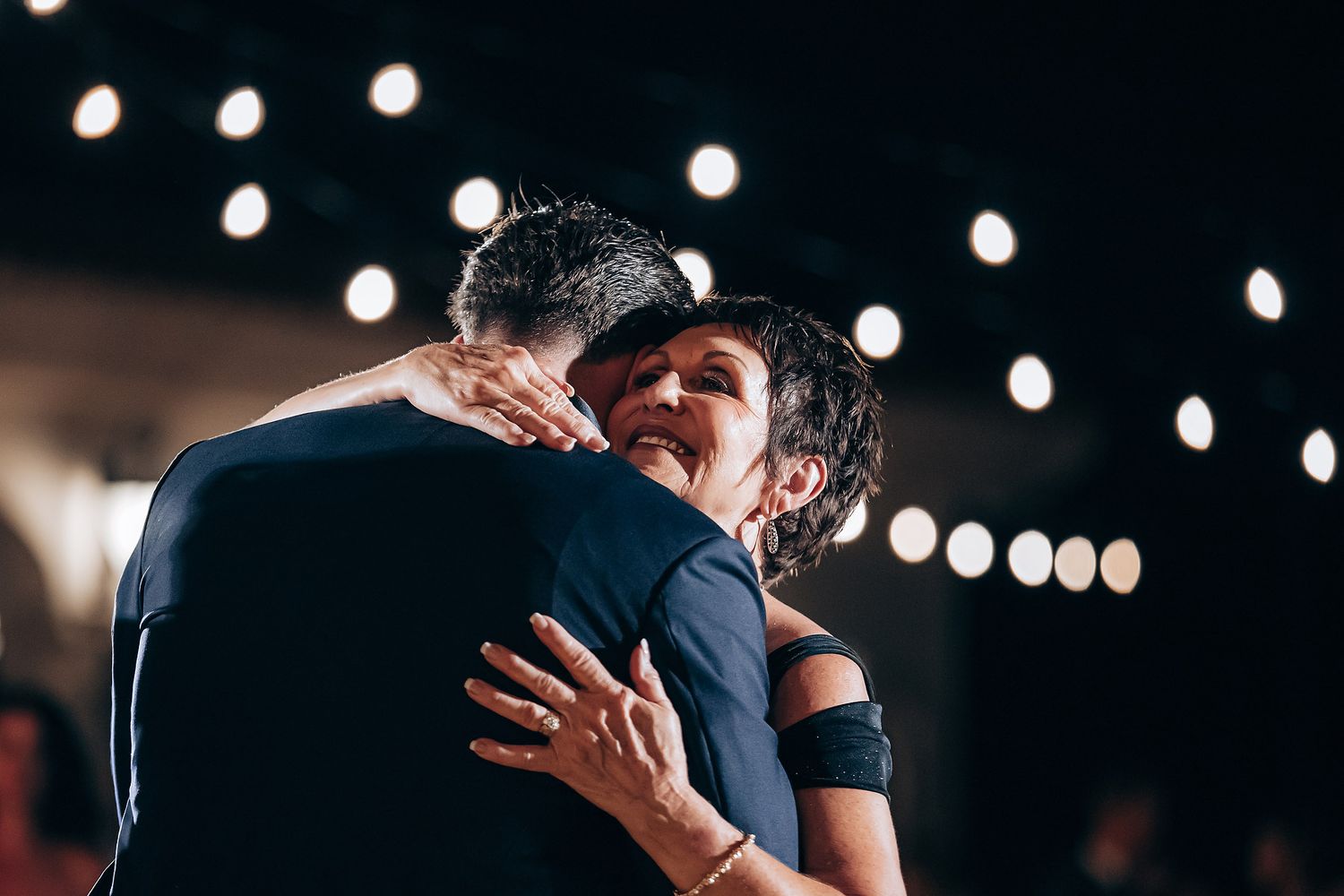 Wedding guests dancing together under string lights at an evening reception celebration.