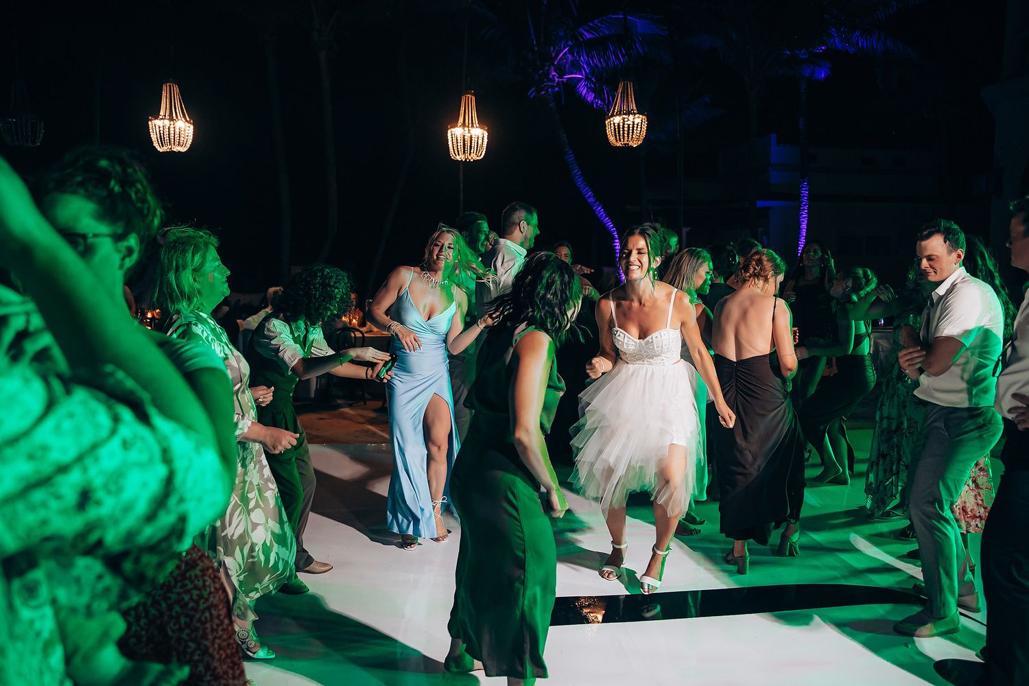 Wedding reception guests dance on a dimly lit dance floor illuminated by green and blue lighting effects.