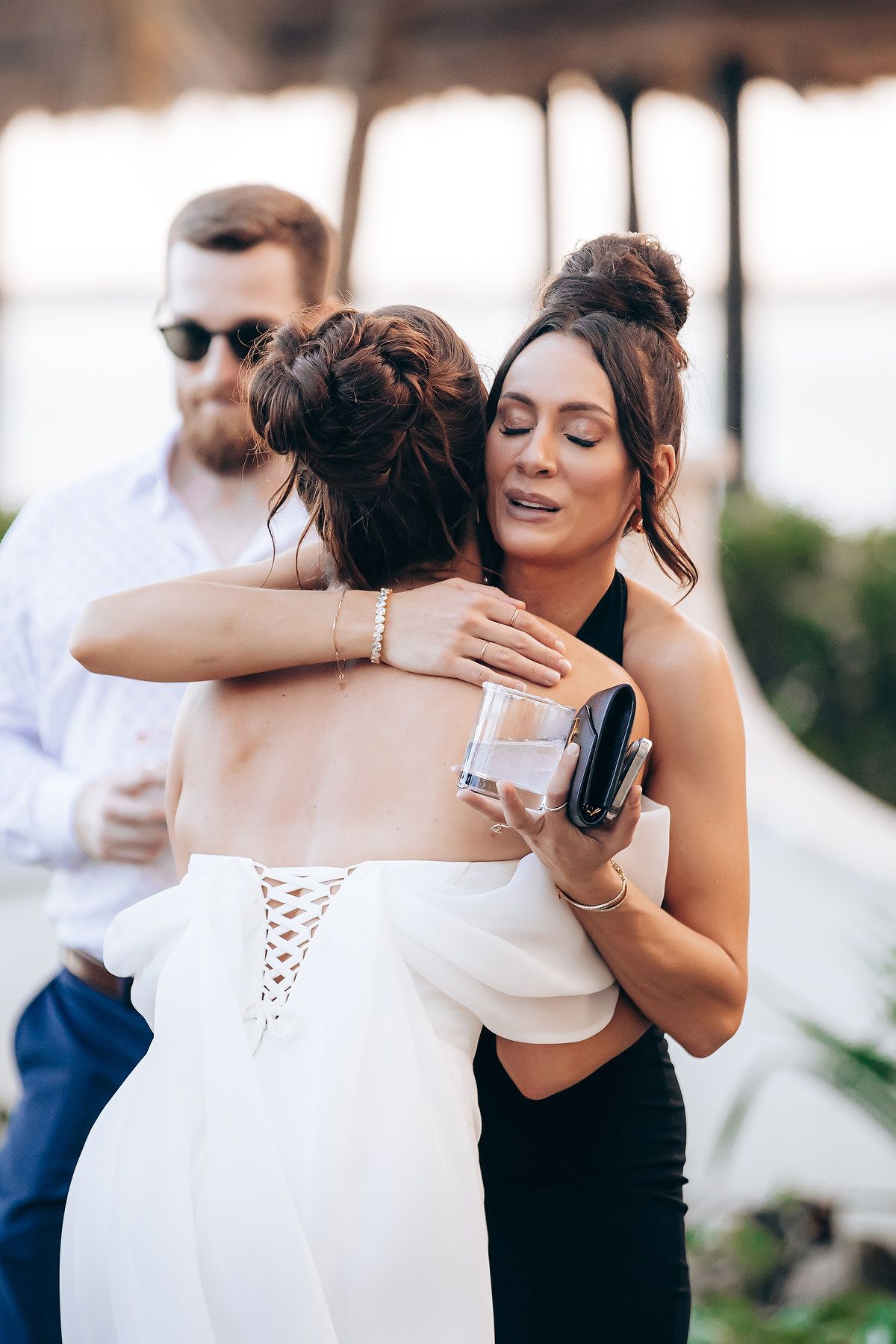 Two women share an emotional embrace during a wedding celebration outdoors.