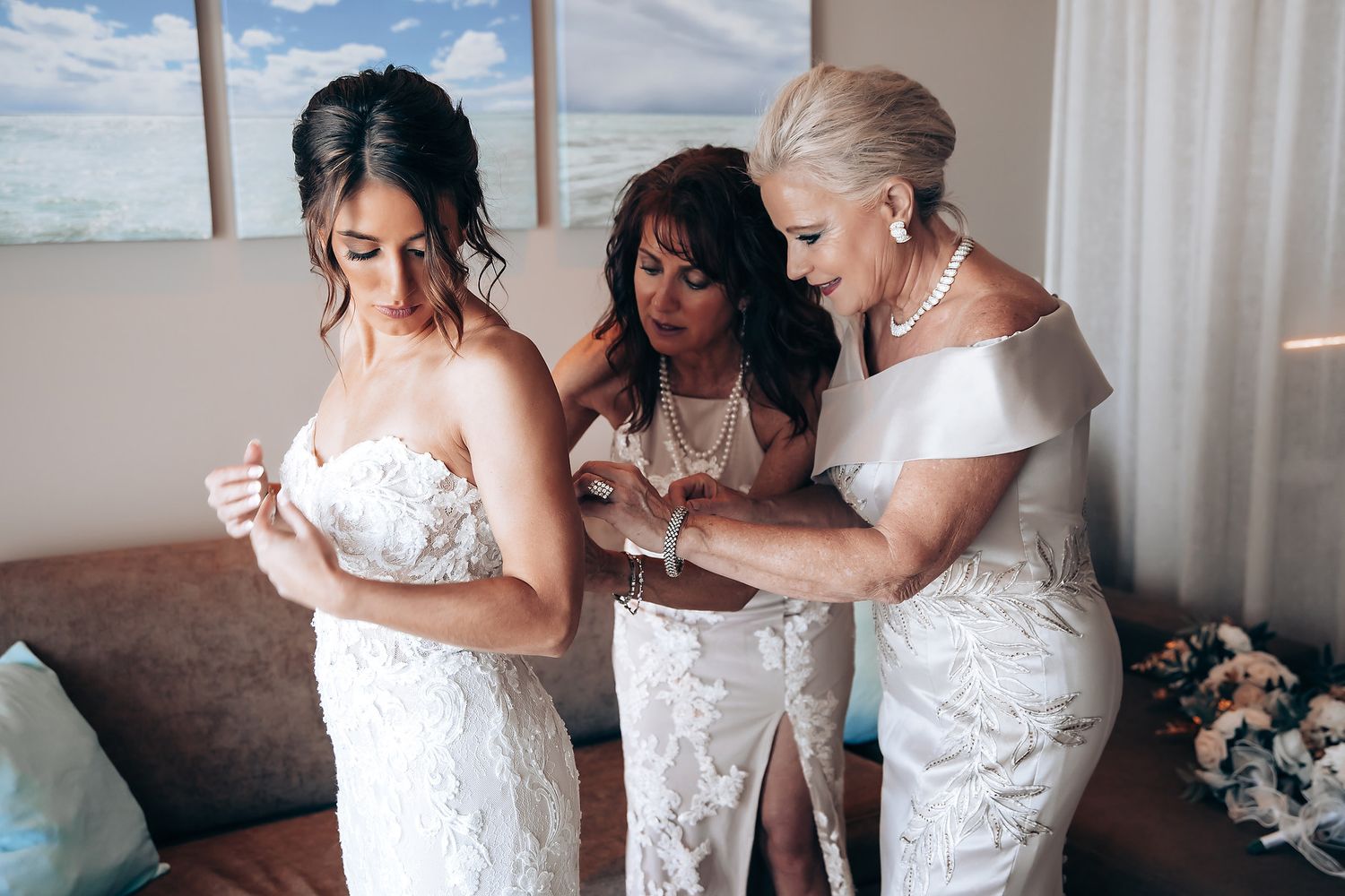 Elegant white wedding dress being adjusted and fitted in a sunlit room with neutral decor.