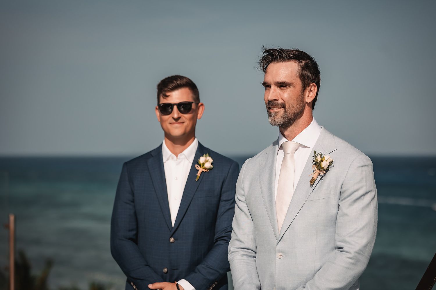 Groomsmen in navy and grey suits pose together by the ocean.