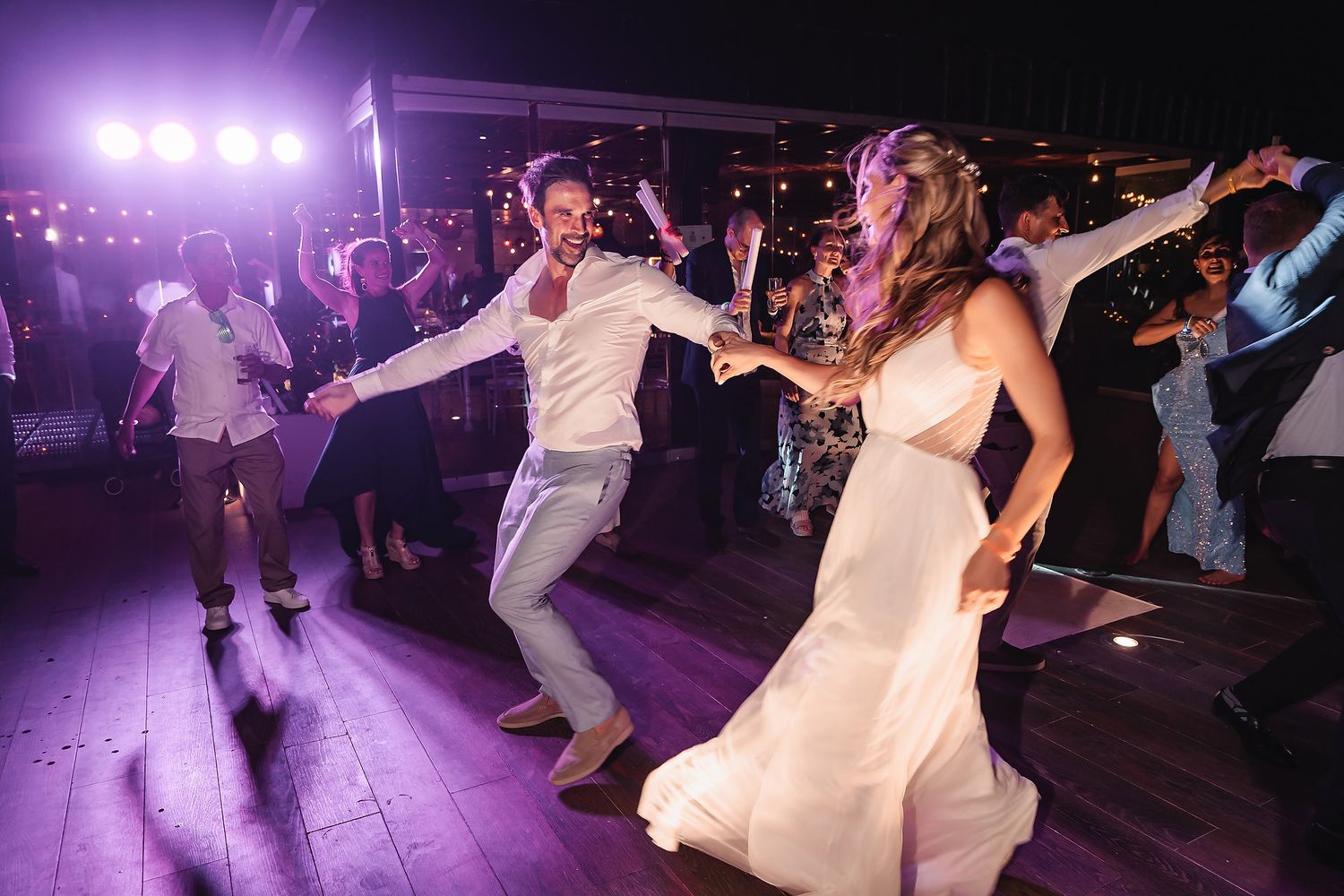 Wedding guests dancing energetically on a dimly lit dance floor with purple lighting effects.