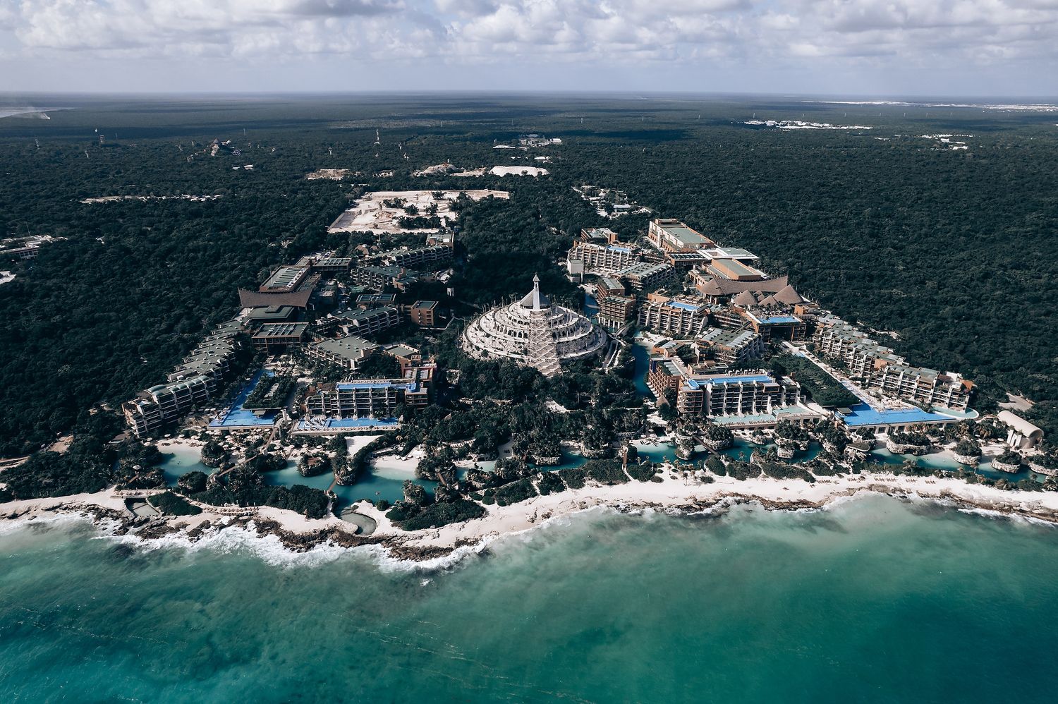 Aerial view of luxury beachfront resorts and hotels along turquoise Caribbean coastline surrounded by tropical forest.