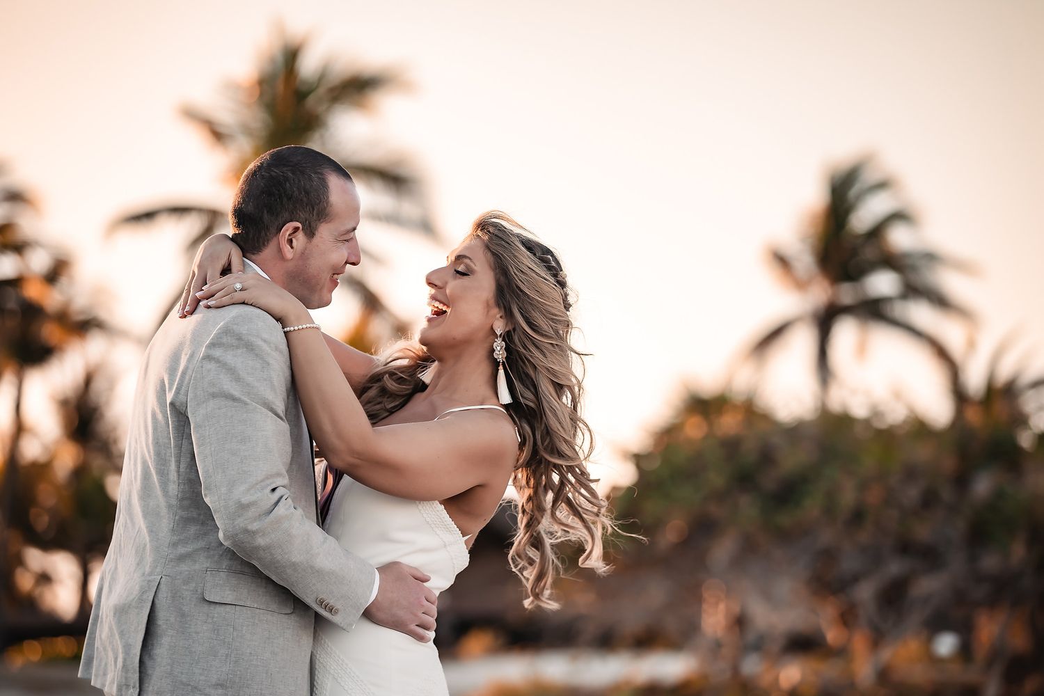 Romantic sunset moment at beach wedding with palm trees silhouetted in background.