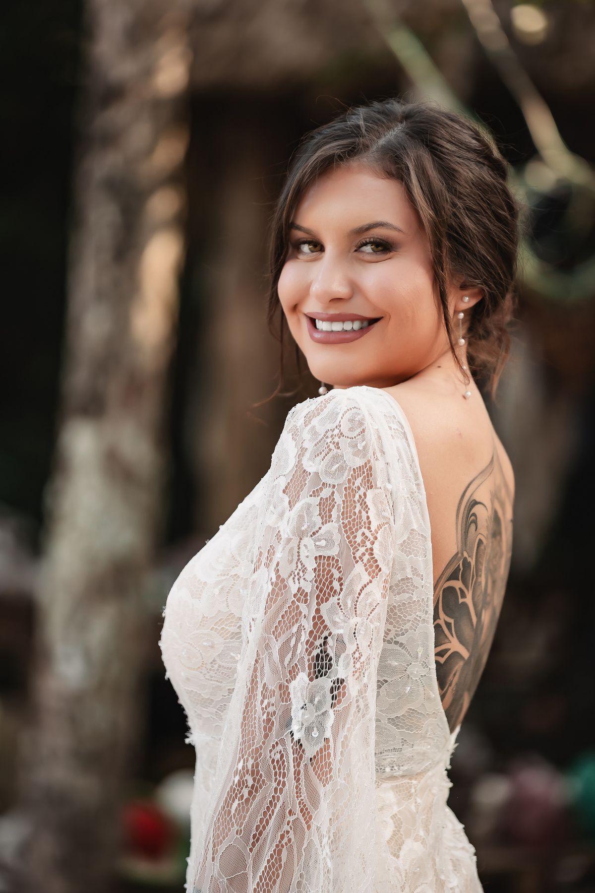 A bride in a delicate lace wedding dress shows off intricate back details and tattoo artwork.