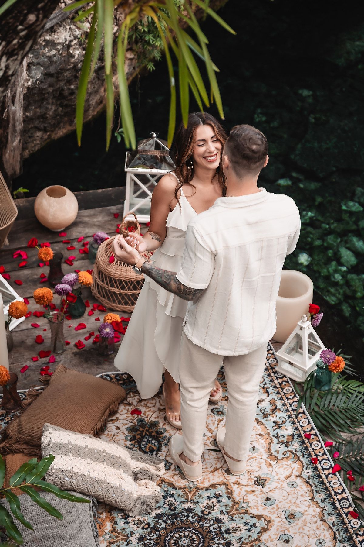 A romantic couple dancing together on a decorated patio with lanterns and flower petals against a natural backdrop.