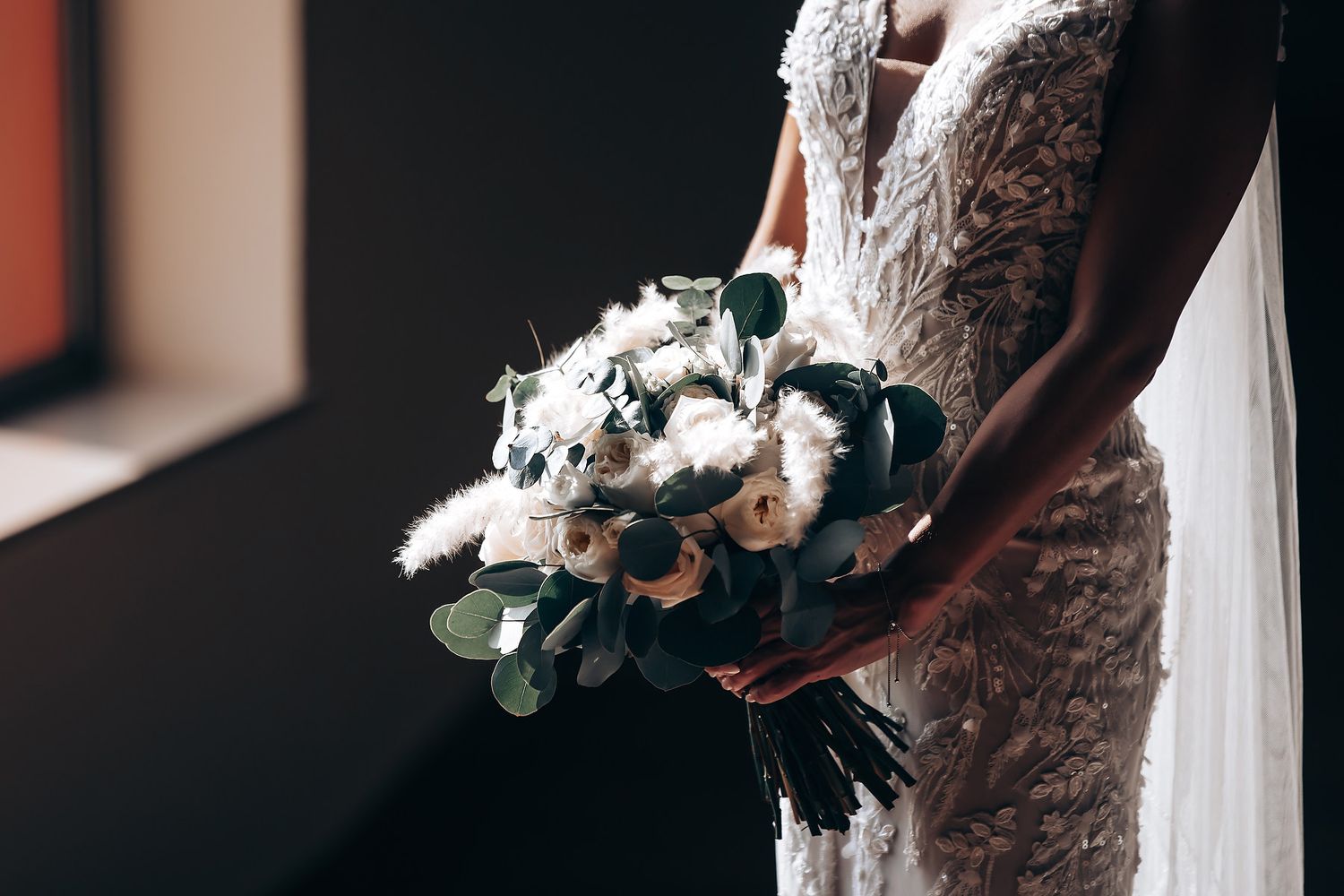 A wedding dress hangs elegantly against a dark background with delicate floral details visible.
