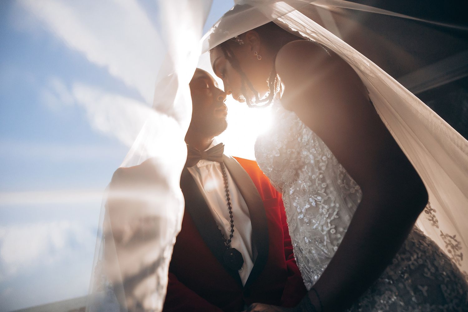 Silhouetted couple embraces in romantic backlit pose with sunlight streaming through sheer fabric.