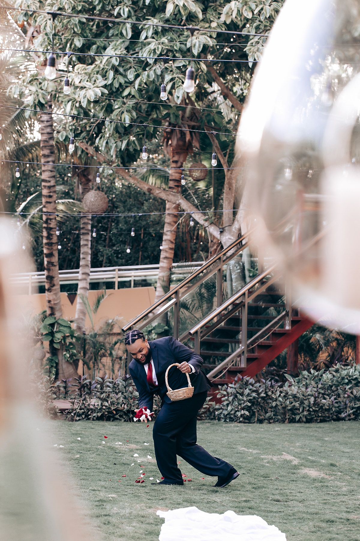 A couple performs a romantic dance pose on a grassy lawn surrounded by palm trees and foliage.