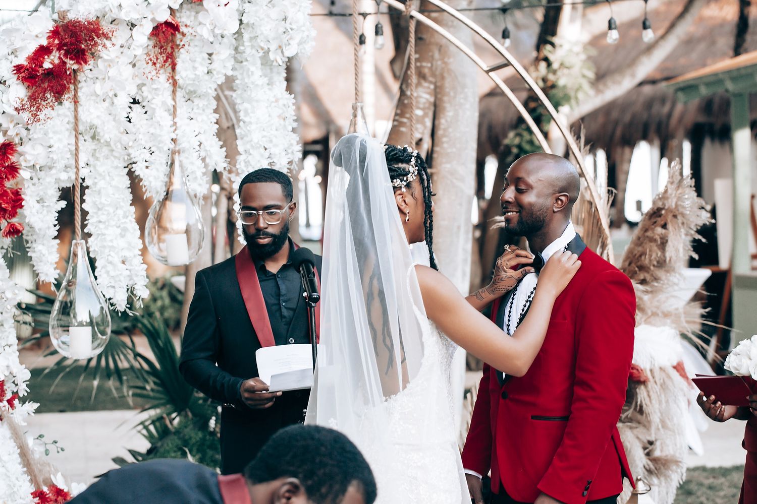 Wedding guests in formal attire celebrate outdoors under decorative white hanging elements.