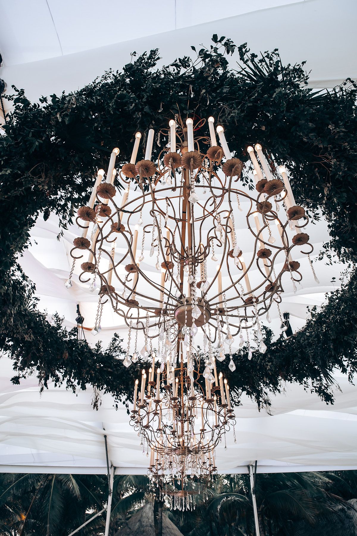 Elegant crystal chandeliers hang from a white tent ceiling at an outdoor wedding reception venue.
