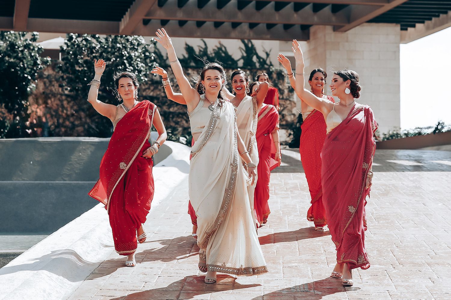 Bridesmaids in red dresses dancing with bride in white gown during outdoor celebration.