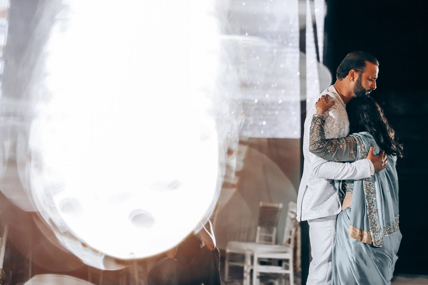 A couple shares an intimate dance moment under bright stage lighting at an event.