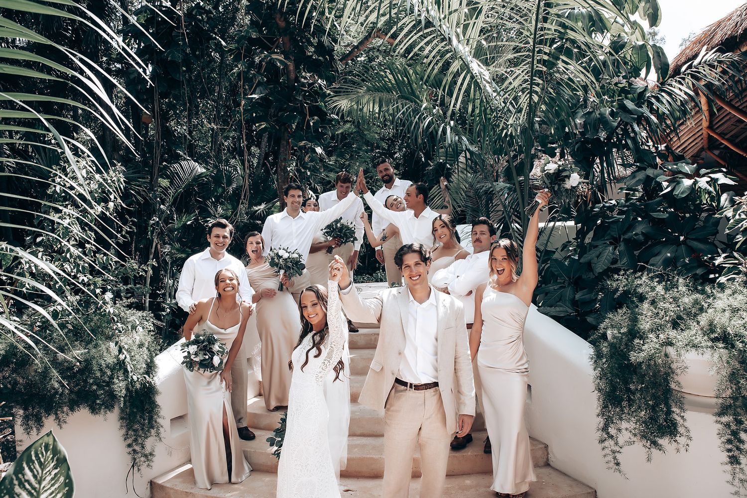 Wedding guests in white and beige attire gathered at an outdoor tropical venue.