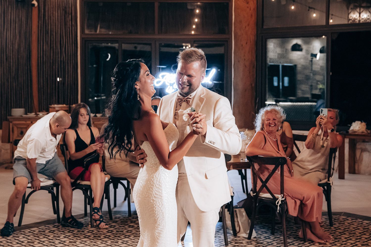 Wedding reception dance in a rustic venue with string lights and wooden beams.