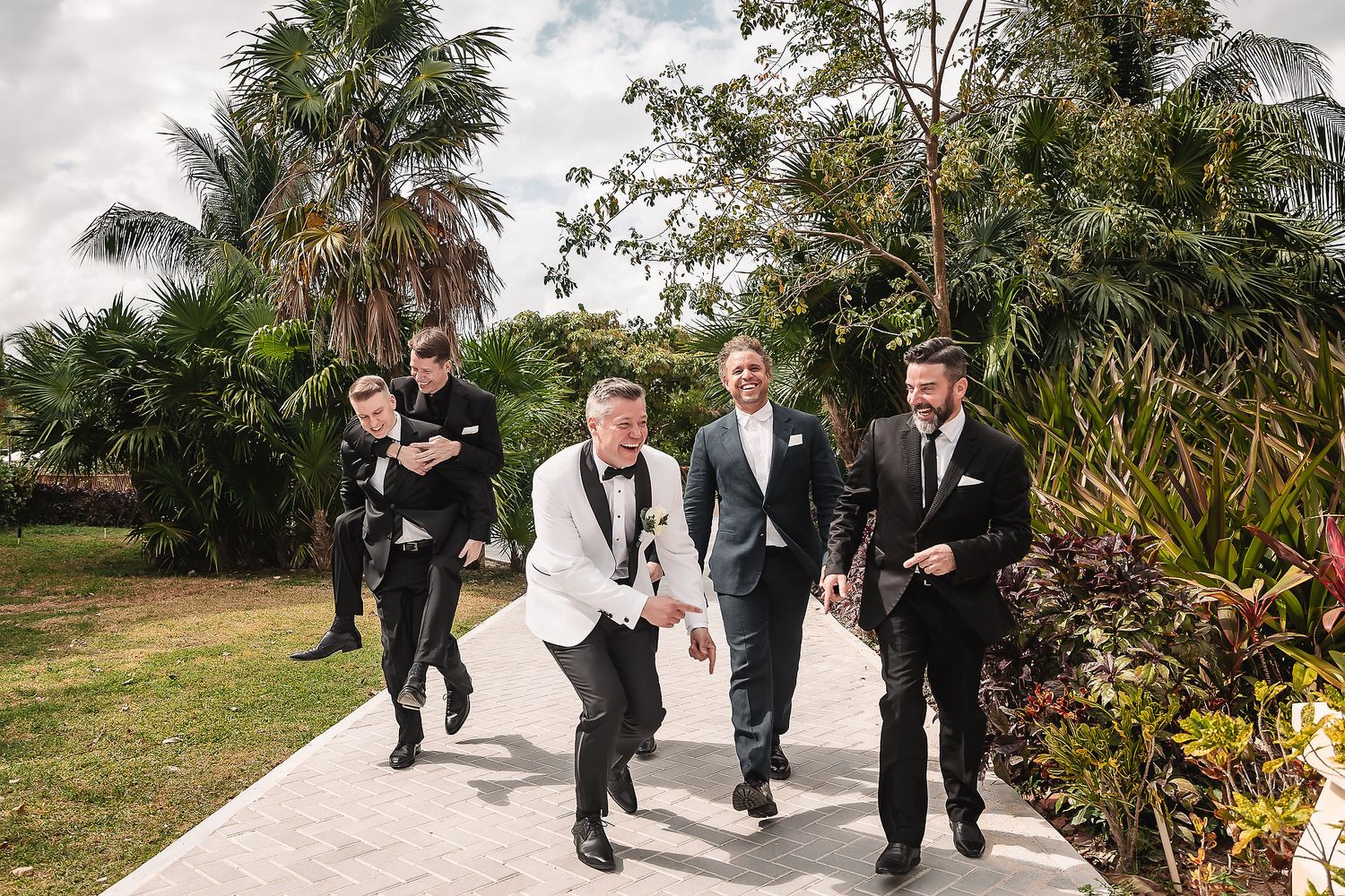 Wedding party members walking along tropical garden path with palm trees.