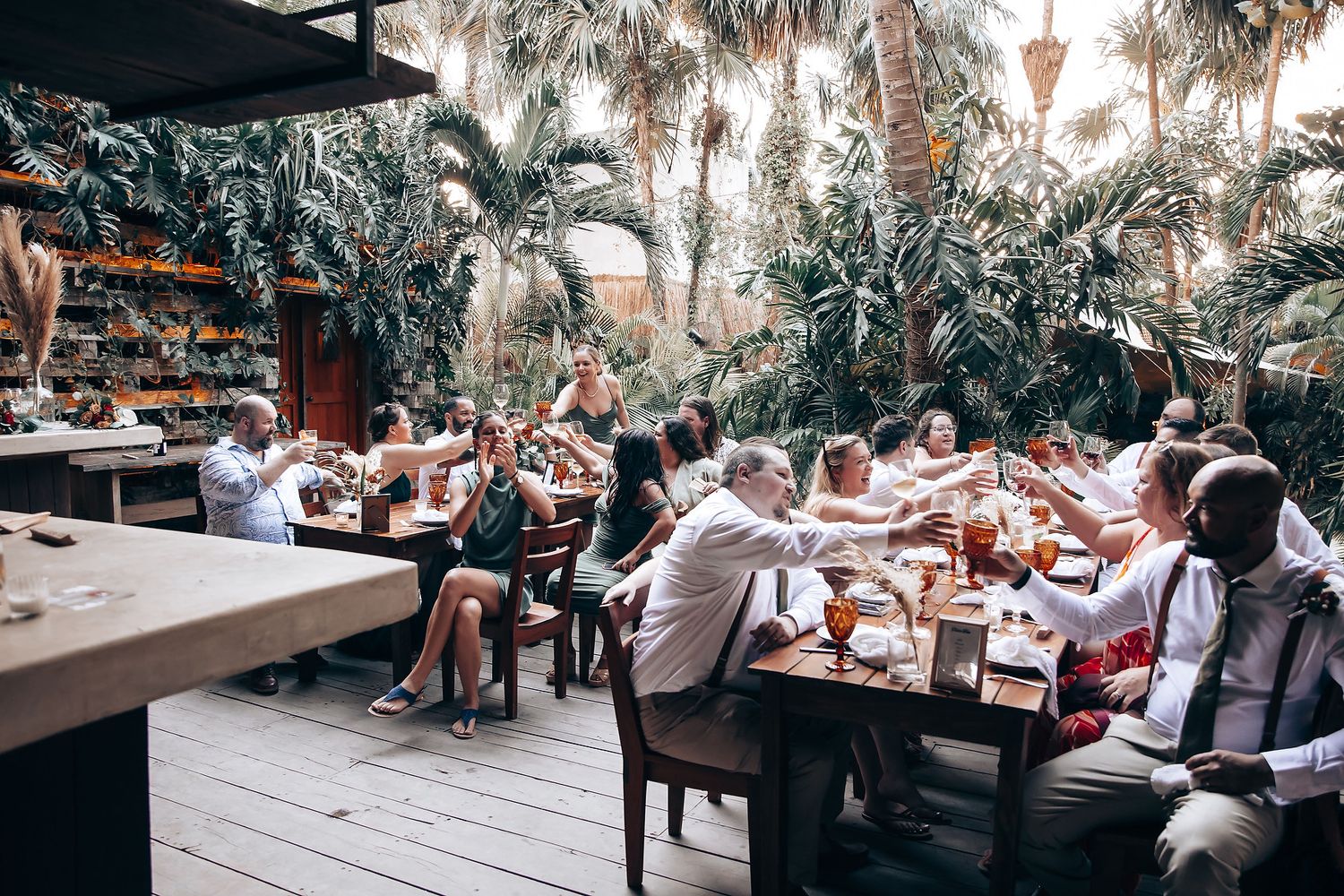 Wedding guests enjoying an outdoor reception dinner under palm trees and string lights at dusk.