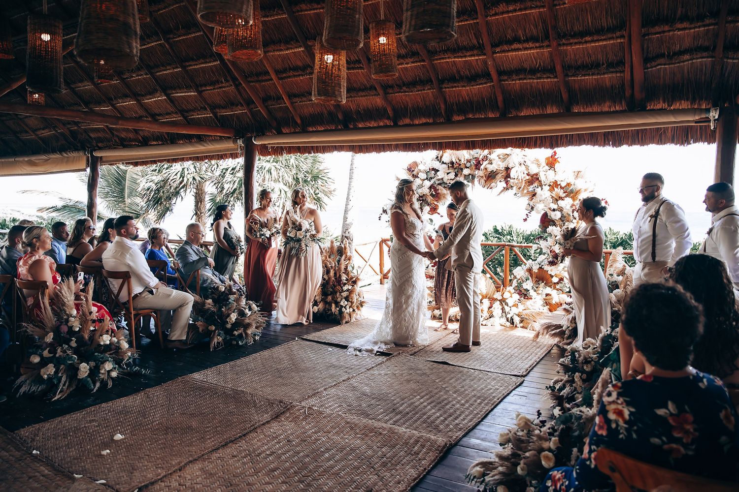 Panoramic view of wedding guests seated in an open-air pavilion by the beach.